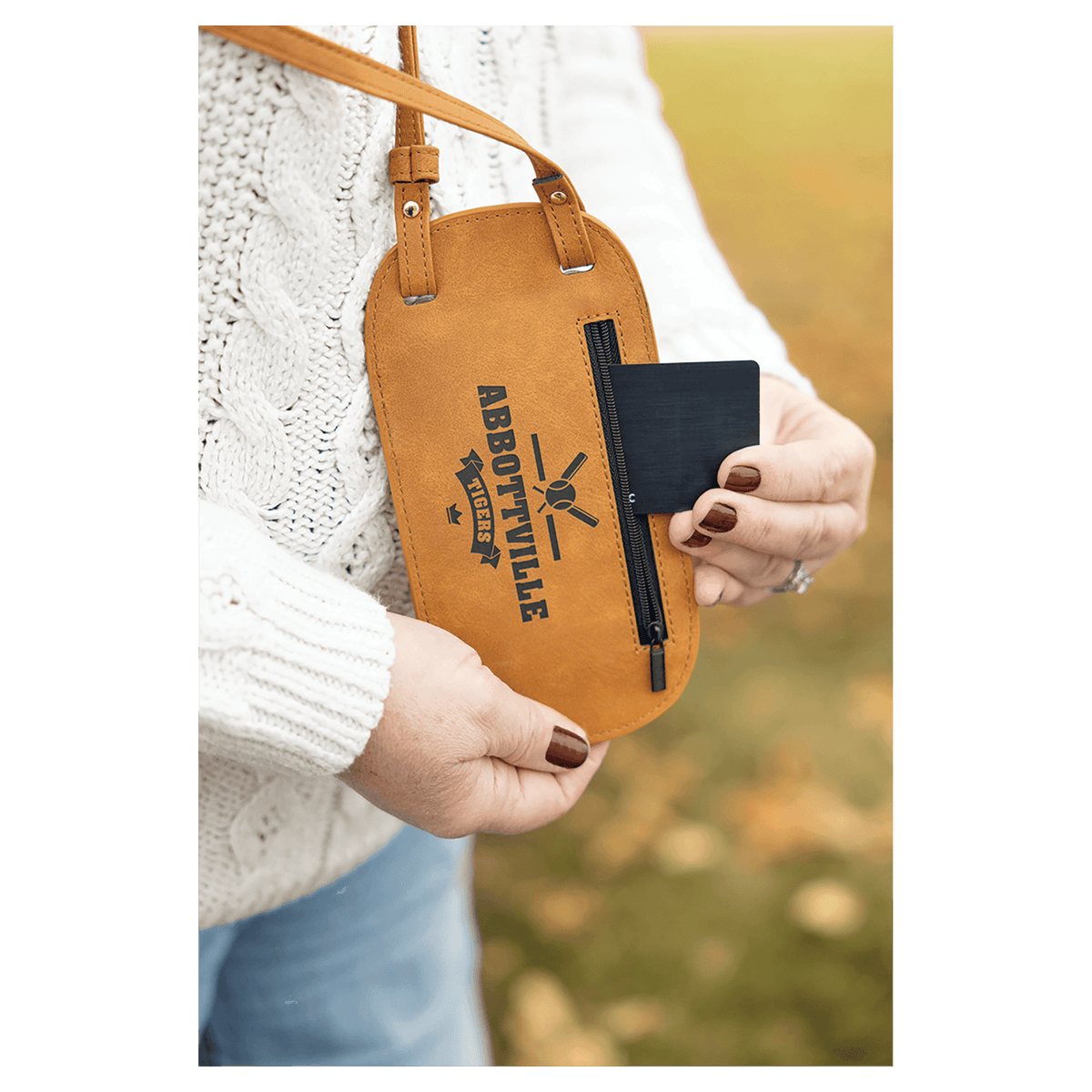 Close-up of a person wearing a tan custom phone bag, pulling a black card from the side zipper pocket.