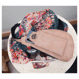 A beige crossbody bag holding a phone sits on a round white table next to a floral scarf, sunglasses, and a pen.