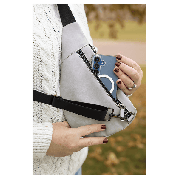 Person in a white sweater pulls a blue phone from a light grey crossbody bag against an autumn background.