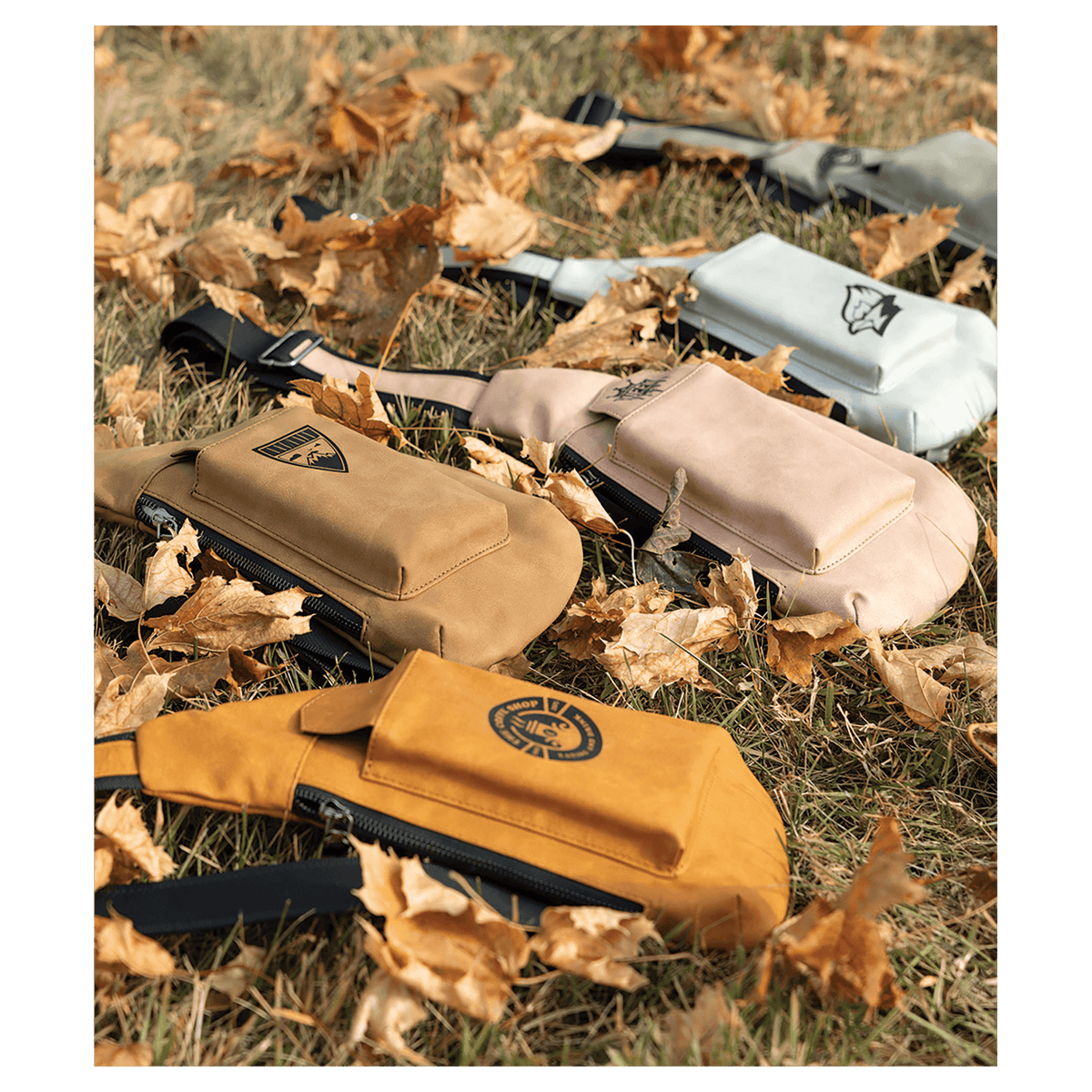 Yellow, tan, beige, and white crossbody bags with front pockets resting on dry grass and autumn leaves.