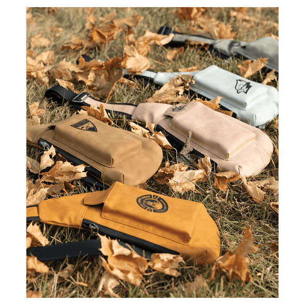 Yellow, tan, beige, and white crossbody bags with front pockets resting on dry grass and autumn leaves.
