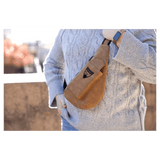 Person in a chunky grey sweater wears a brown crossbody sling bag outdoors in bright sunlight.