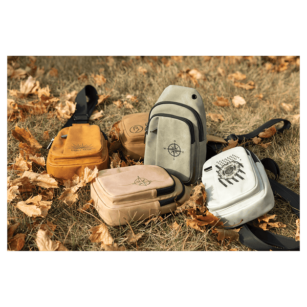 Five small crossbody bags in yellow, brown, gray, tan, and white with black straps scattered on dry autumn grass.