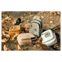 Four small sling bags in yellow, tan, grey, and white with black graphics, resting on dry grass and autumn leaves.