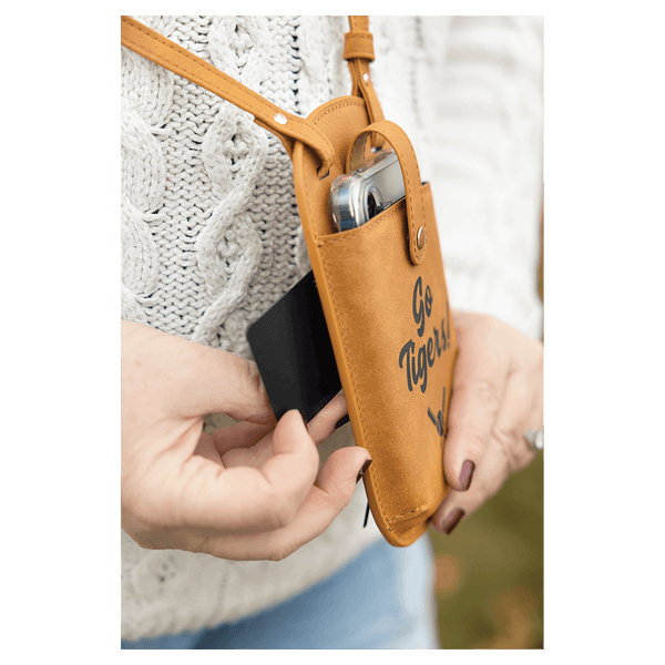 Hands pull a card from a brown crossbody phone bag printed with "Go Tigers!" against a white sweater and blue jeans.