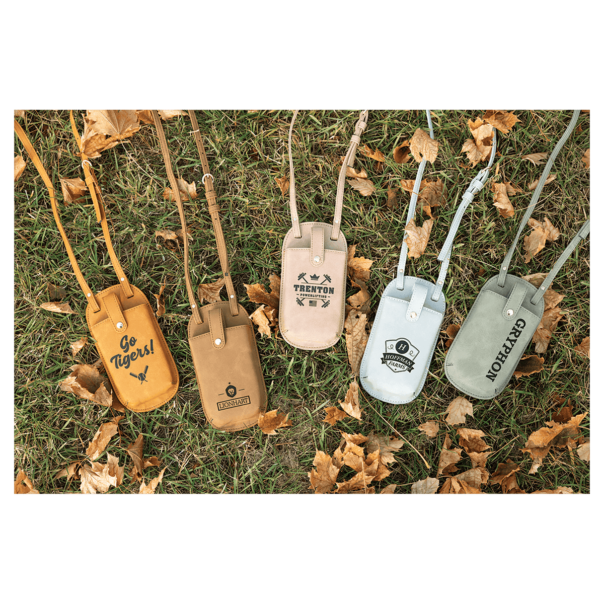 Five personalized phone bags in yellow, brown, beige, blue, and green resting on grass with autumn leaves.