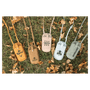 Five personalized phone bags in yellow, brown, beige, blue, and green resting on grass with autumn leaves.