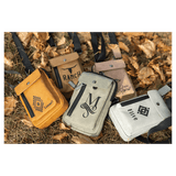 Four crossbody bags in yellow, tan, grey, and white with black graphics, resting outdoors on dry autumn leaves.