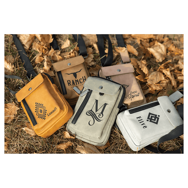 Four crossbody bags in yellow, tan, grey, and white with black graphics, resting outdoors on dry autumn leaves.