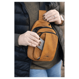 Person in a black vest wearing a mustard yellow sling bag, taking a silver card out of its front slip pocket.