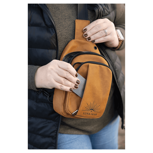 Person in a black vest wearing a mustard yellow sling bag, taking a silver card out of its front slip pocket.