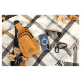 Mustard yellow sling bag, blue phone, black sunglasses, and keys flat on a grey and white plaid blanket with leaves.