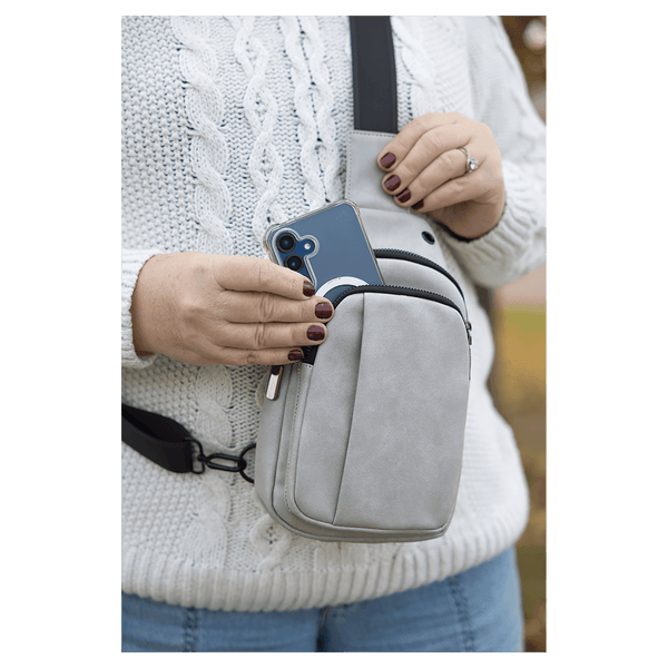 Person wearing a white sweater taking a blue smartphone out of a light gray crossbody bag worn on their chest.