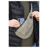 Person wearing a black vest pulls a blue smartphone from an olive green crossbody bag.