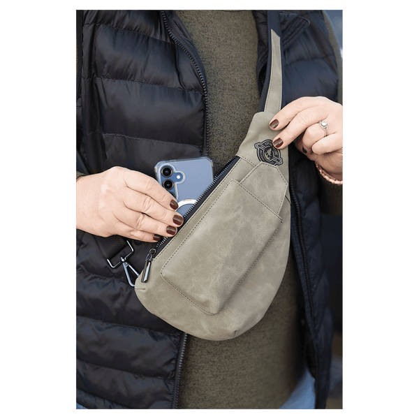Person wearing a black vest pulls a blue smartphone from an olive green crossbody bag.
