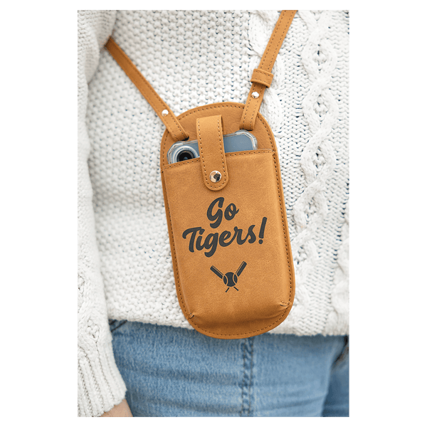 A brown crossbody phone bag printed with "Go Tigers!" and baseball bats, worn over a white sweater and blue jeans.
