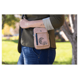 Pink bag with flap pocket, snap hardware, and side zipper worn at the hip by a person outdoors in a green park.