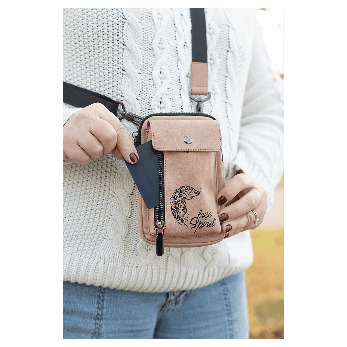 Person outdoors wearing a pink crossbody bag with black strap, metal clips, and side zipper, pulling out a card.