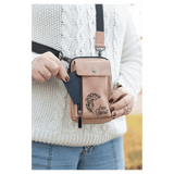Person outdoors wearing a pink crossbody bag with black strap, metal clips, and side zipper, pulling out a card.