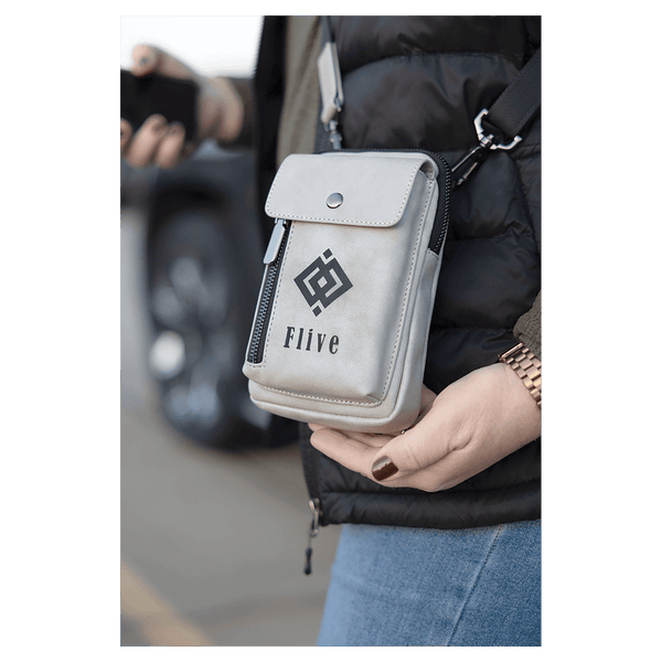 Light grey crossbody bag with a front snap flap, vertical zipper, and black strap, worn over a black puffer vest.